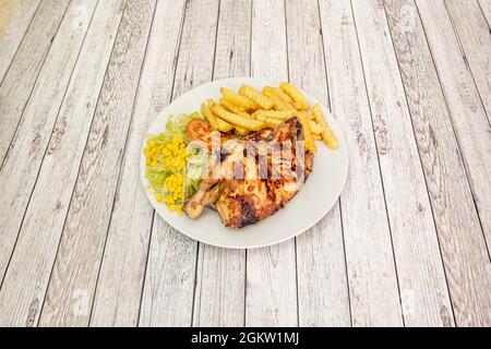 Porzione di pollo arrosto con patate e insalata con lattuga e mais dolce su piatto bianco Foto Stock