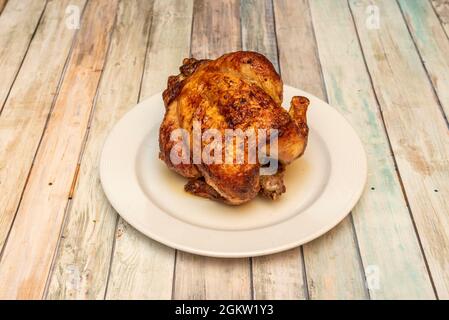 Pollo intero arrostito in una rotisserie con pelle molto croccante su piatto bianco e tavolo in legno Foto Stock