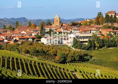 Vista dei vigneti autunnali sulla collina e piccolo paese sullo sfondo in Piemonte, nel Nord Italia. Foto Stock