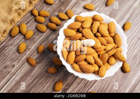 Vista dall'alto delle mandorle in una ciotola bianca su sfondo di legno Foto Stock