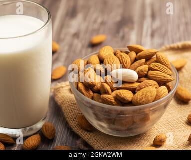 Noci di mandorla sbucciate in una ciotola di vetro e un bicchiere d'acqua su tavola di legno Foto Stock