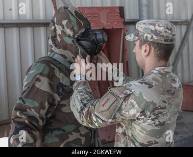 Amar Misimovic assiste il PFC dell'esercito degli Stati Uniti. Dylan Vickers nel mettere sul suo MOPP 4 abbigliamento protettivo alla Mihail Kogalniceanu Air base in Romania, 9 luglio 2021. MOPP 4 è composto da una maschera protettiva, un supporto per maschera e un cappotto JSLIST, pantaloni, guanti e stivali. Lo spiegamento di forze americane pronte e credibili nei combattimenti in Europa a sostegno della risolutezza atlantica è la prova del forte e inremotabile impegno degli Stati Uniti nei confronti della NATO e dell'Europa. Foto Stock