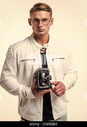 Il desiderio incontra un nuovo hobby. Bel ragazzo tenere retro fotocamera isolato su bianco. I giovani fotografi indossano occhiali in stile casual. Attrezzatura fotografica Foto Stock
