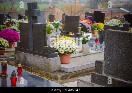 Candele brucianti, fiori di crisantemo, simboli e altri ornamenti su tombe nel cimitero durante il giorno di tutti i Santi Foto Stock