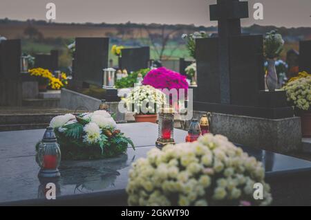 Candele brucianti, fiori di crisantemo, simboli e altri ornamenti su tombe nel cimitero durante il giorno di tutti i Santi Foto Stock