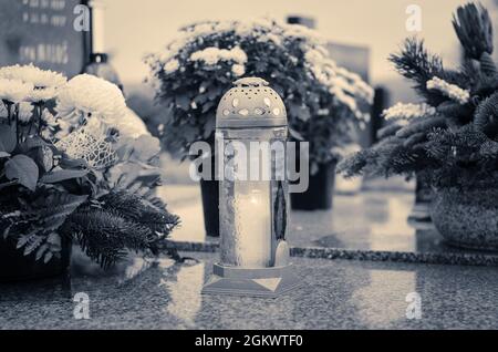 Candele brucianti, fiori di crisantemo, simboli e altri ornamenti su tombe nel cimitero durante il giorno di tutti i Santi Foto Stock