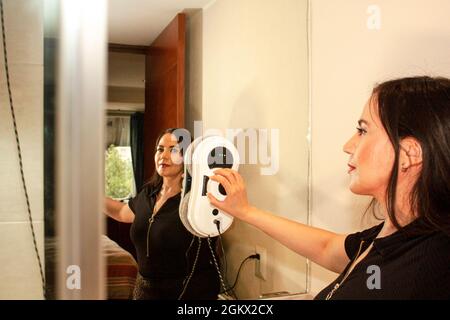 Lavorando a casa pulizia specchio in bagno, donna posiziona robot sullo specchio per pulire il vetro e dare il comando di avvio alla pulizia assistente a casa in M. Foto Stock