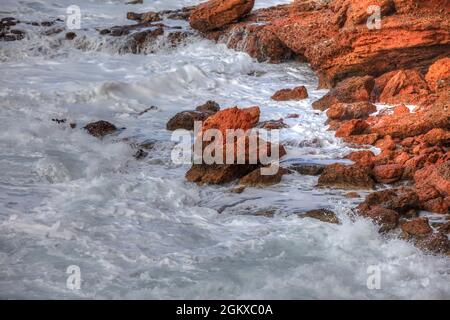 Red Coast Rocks. Acqua salata con schiuma sulla costa dell'isola di Syros, Grecia. Foto Stock