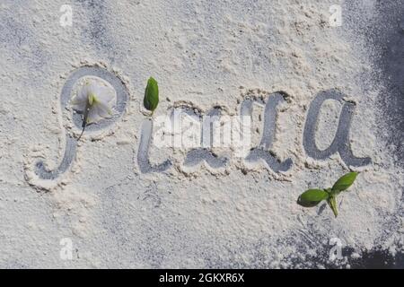 La parola Pizza, scritta in farina su un tavolo nero con foglie di basilico. Menu. Foto Stock