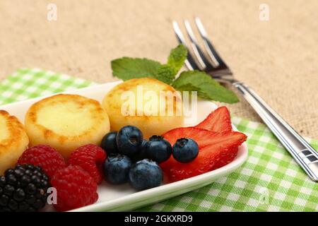 Primo piano porzione di dessert al formaggio europeo di quark pancake con frutta sul tavolo, vista ad angolo alto, prospettiva personale Foto Stock