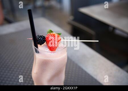 Closeup orizzontale di frullato fresco con fragola e mora in cristallo servito in bar all'aperto su tavolo grigio con tavolo vuoto con due Foto Stock