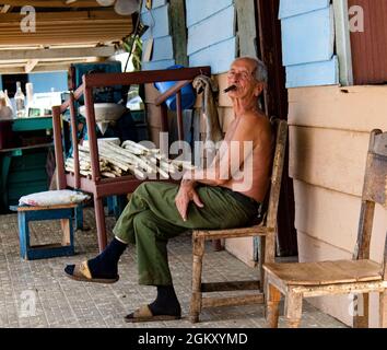 L'uomo siede nel portico anteriore della casa che fuma un sigaro cubano a Trinidad, Cuba. Foto Stock