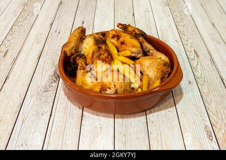 Pollo tritato arrostito in forno in una ciotola di terracotta accompagnato da patatine fritte su un tavolo di legno chiaro Foto Stock