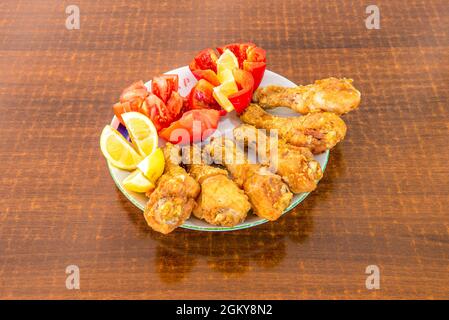 Piatto rotondo con cosce di pollo fritte croccanti guarnite con pomodori, peperoni e limoni Foto Stock