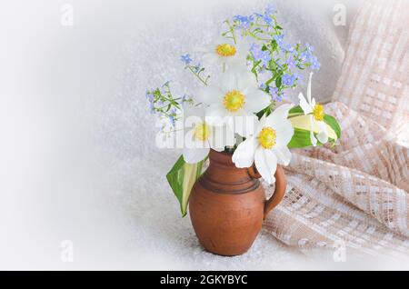 Un piccolo bouquet di anemoni e scordami-me-not in un vaso di argilla su sfondo chiaro Foto Stock