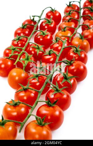 mazzo di pomodori ciliegini maturi con le loro braccia legnose su tavola bianca Foto Stock