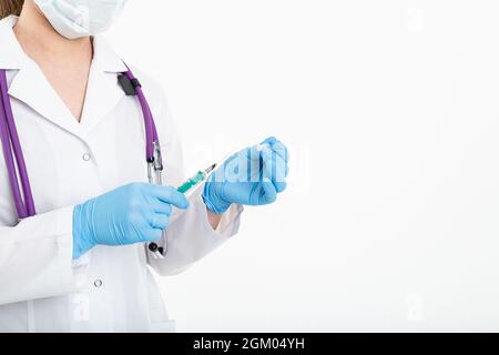 Un giovane infermiere in una maschera apre una siringa su sfondo bianco in un cappotto bianco, per fare una vaccinazione, un'iniezione. Il concetto di vaccinazione e. Foto Stock