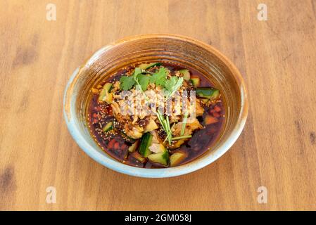 Ramen di pollo piccante con pezzi di zucchine, arachidi, prezzemolo e semi di sesamo in ciotola di ceramica Foto Stock