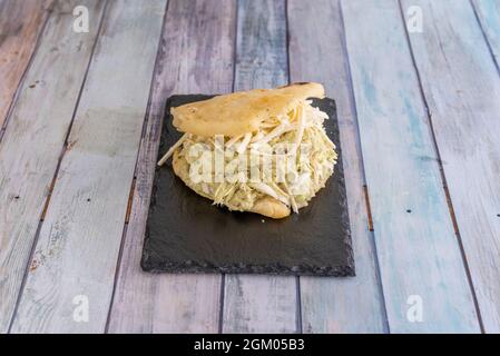 Arepa venezuelana farcita con pepiada regina con pollo, avocado, maionese e formaggio con pasta di farina di mais su piatto di ardesia nera Foto Stock