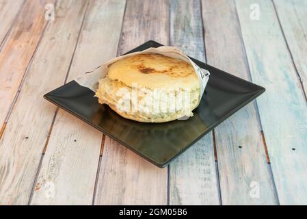 La regina venezuelana pepiada arepa con maionese, avocado, formaggio, pollo grattugiato e pane di farina di mais su piatto nero Foto Stock