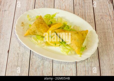 Porzione di samosa vegetale servita in un ristorante indù con lattuga iceberg e una fetta di limone con pepe e curry macinato Foto Stock