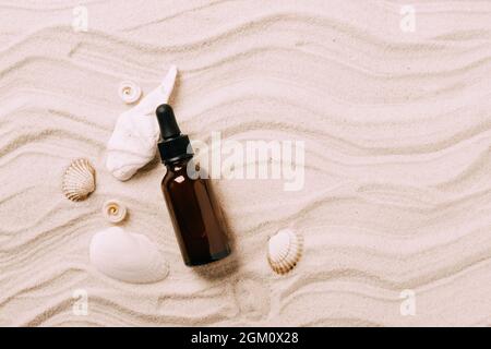 Bottiglia di vetro con olio essenziale siero prodotto cosmetico sfondo di spiaggia di conchiglie sabbia, presentazione del prodotto Foto Stock