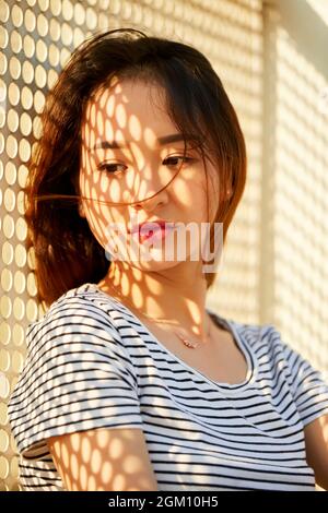 Ritratto di giovane e pensiva bella donna con rete d'ombra sul suo volto in piedi all'aperto Foto Stock
