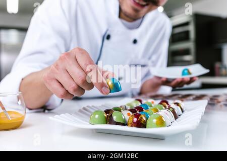 Giovane uomo latino chocolatier in cappello chef in piedi con cioccolatini messicani caramelle su piatto in una cucina commerciale in Messico America Latina Foto Stock