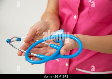 Medico femminile in uniforme medica rosa tiene stetoscopio nelle sue mani. Assicurazione sulla vita e sulle malattie. Esami professionali. Medicina e salute. Healt Foto Stock