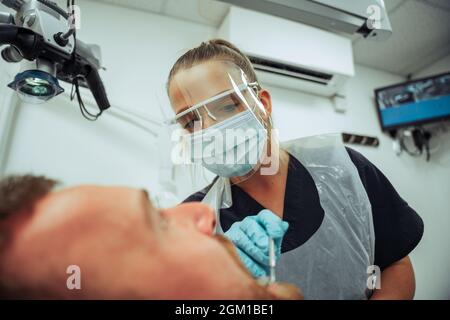 Caucasico cliente seduta dentista sedia mentre l'infermiere femminile opera su denti rotti Foto Stock