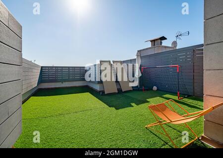 Terrazza privata con lettini da mare, porte da calcio per bambini e erba sintetica nelle giornate di sole con cielo blu. Foto Stock