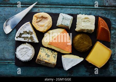 Vista dall'alto di una selezione di formaggi di lusso su una tavola di ardesia con coltello Foto Stock