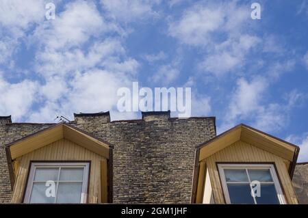 Foto concettuale di casa con finestre dormitorio vintage in legno sul tetto della costruzione contro il cielo blu con le nuvole nella città vecchia in Lituania. Appartamenti estetici nella mansarda contro skyline Foto Stock