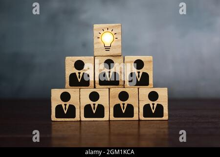 Lavoro di squadra, brainstorming e concetto creativo. Blocco cubo di legno con lampadina e simboli umani Foto Stock