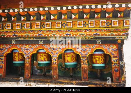 Parete ornata dipinta con ruote di preghiera all'interno di singole nicchie ad arco che mostrano abile carpenteria e decorazioni di architettura tradizionale in Bhutan Foto Stock