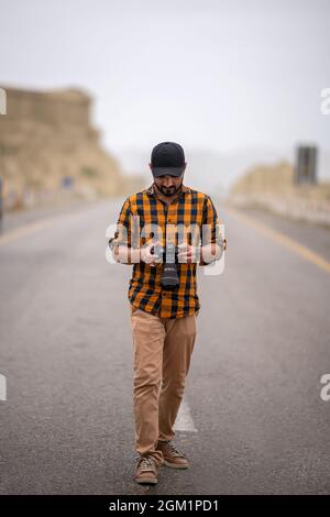 Uomo premuroso che tiene la macchina fotografica, fotografo cammina all'aperto con la sua macchina fotografica Foto Stock