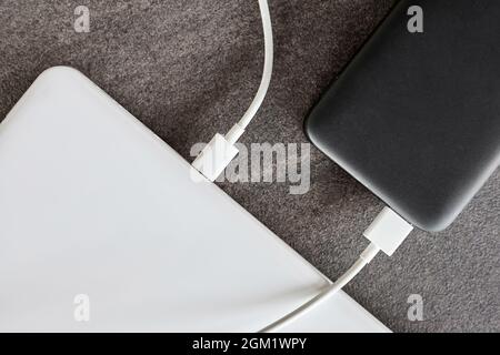Power Bank ricarica un computer portatile tramite cavo USB di tipo C su sfondo grigio in pietra Foto Stock