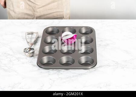 Cottura di cupcake al cioccolato. Fodera teglia per cupcake in metallo con fodere per cupcake. Foto Stock
