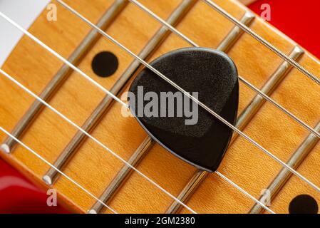 Dettaglio del collo e delle corde di una chitarra elettrica rossa, con un plectrum nero chiamato anche mediatore Foto Stock