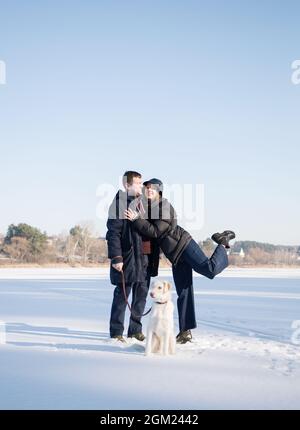 l'uomo felice e la donna amamored abbracciano, camminano il cane nella neve in inverno. sentimenti teneri, umore festoso, gioia di rapporto. San Valentino insieme Foto Stock