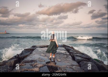 Dietro la giovane donna asiatica in piedi e posando su rocce jetty e onda colpire sulla spiaggia Jumunjin a Gangneung, Corea del Sud Foto Stock