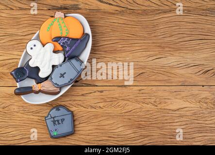 Halloween pani di zenzero, zucca, lapide, cappello di strega, gatto nero su un piatto su tavola di legno con spazio copia. Foto Stock
