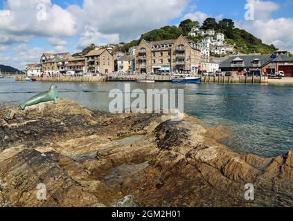 La scultura Nelson the Seal di Suzie Marsh poggiava sulle rocce accanto al fiume Looe con il Quayside of East Looe sullo sfondo. Un monumento a un Foto Stock