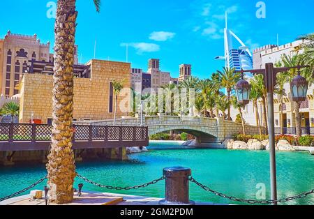 Lo stretto canale del mercato di Souk Madinat Jumeirah con una vista su un ponte di pietra per l'Isola di Fort e guglia di Burj al Arab sullo sfondo, Dubai, UA Foto Stock