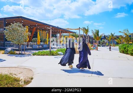 Due donne in abbigliamento musulmano tradizionale (abayah e hijab) camminano la passeggiata della spiaggia di la Mer, Dubai, Emirati Arabi Uniti Foto Stock