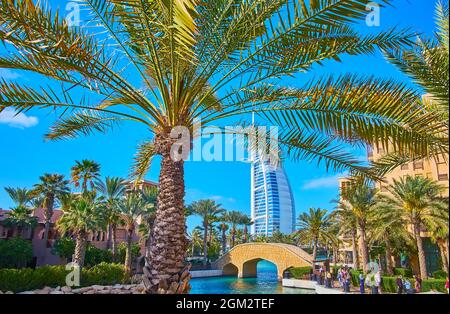 La vista sul canale, il piccolo ponte, i windcatchers del mercato di Souk Madinat Jumeirah e Burj al Arab hotel attraverso i rami di palma, ondeggiare sul vento, D Foto Stock