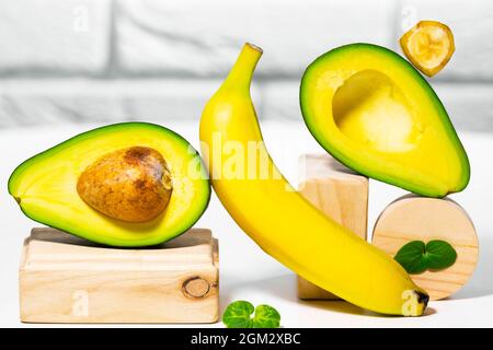 Avocado creativo, banana e micro verde equilibrio legno stand e podi., sfondo bianco, equilibrio sano cibo. Concetto di nutrizione equilibrata Foto Stock