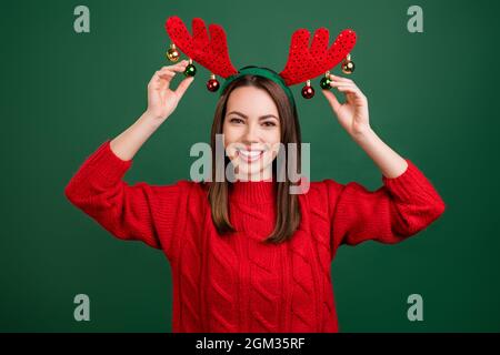 Foto di giovane ragazza felice sorriso positivo toccare palle renna corna vacanza natale decorazione isolato su sfondo verde colore Foto Stock