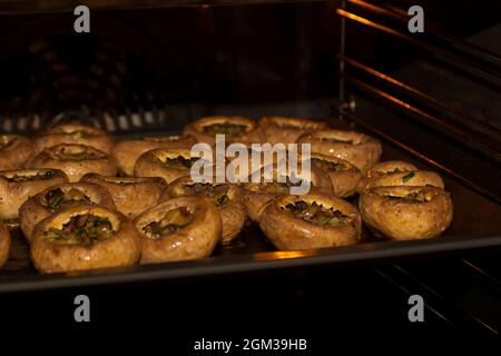 Cottura di funghi con formaggio. Cottura di champignons ripieni di formaggio nel forno elettrico Foto Stock