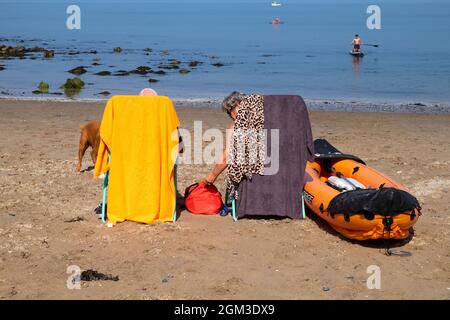 Coppia anziana sulla spiaggia sabbiosa a New Quay a Cerediaion sulla costa gallese con kayak rilassante seduta in sdraio Galles UK KATHY DEWITT Foto Stock